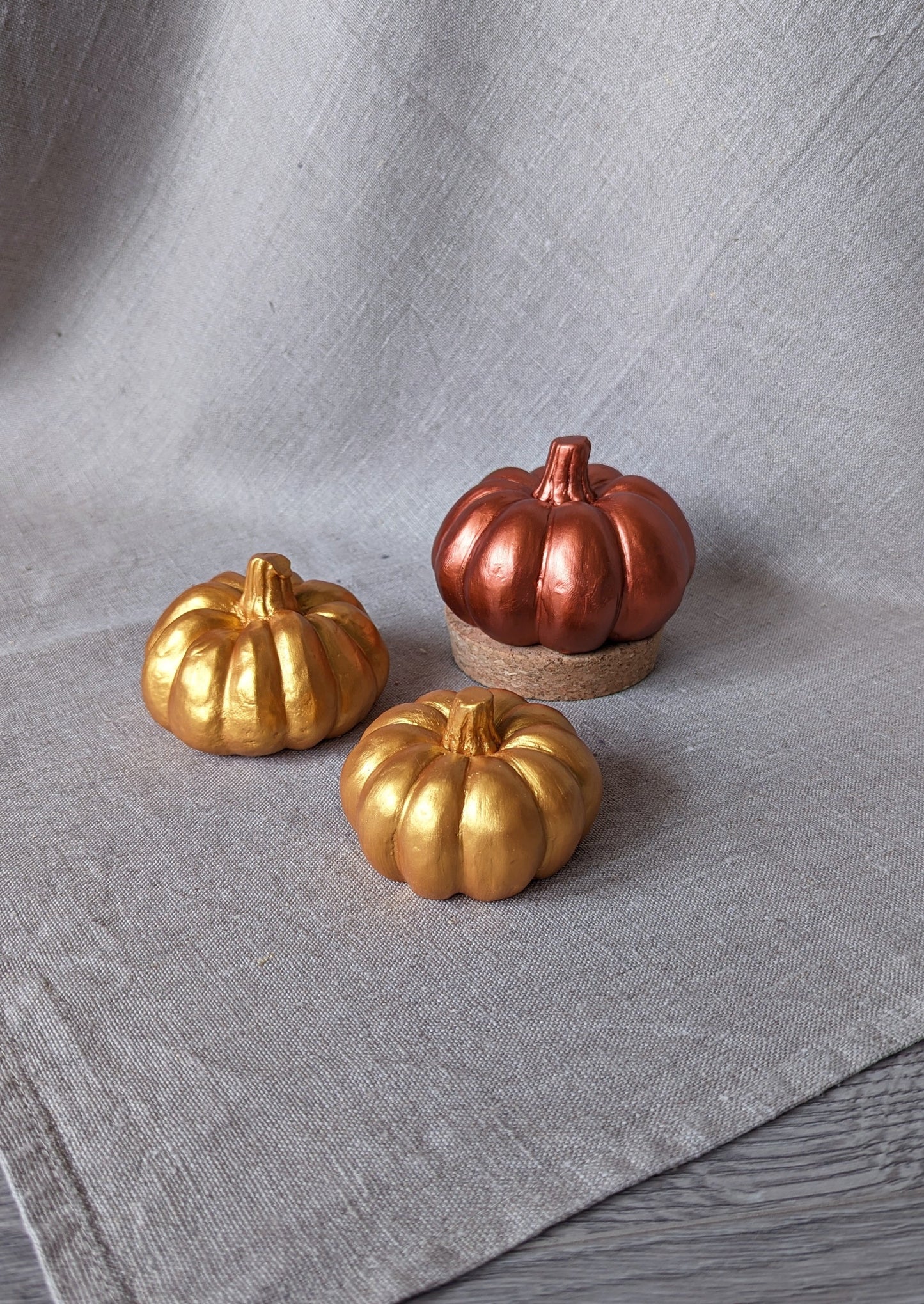 3 concrete pumpkins in 3 sizes and two colours (warm gold and bright copper) in a background of linen fabric.